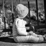 Kleines Kind sitzt an einem Geländer und blickt ins Freie – Symbol für bedingungslose Liebe und tiefe Verbindung