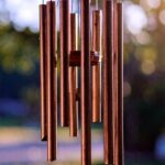 Ein schlichtes Windspiel aus Metallstäben schimmert im Licht – Symbol für Achtsamkeit, Einklang und Rhythmus im Geräusch.